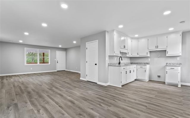 kitchen with light wood finished floors, recessed lighting, white cabinetry, a sink, and baseboards