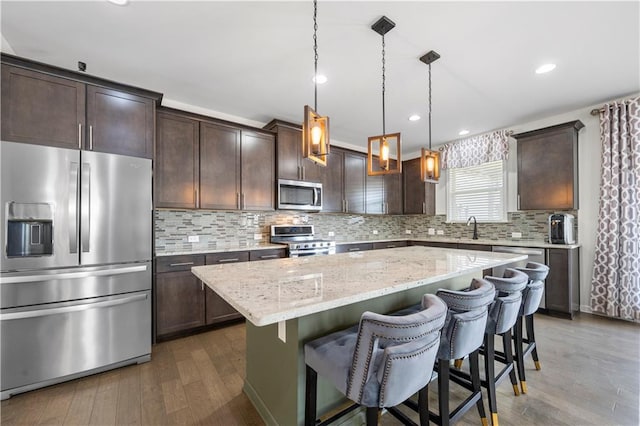 kitchen featuring a center island, dark wood-type flooring, hanging light fixtures, decorative backsplash, and appliances with stainless steel finishes