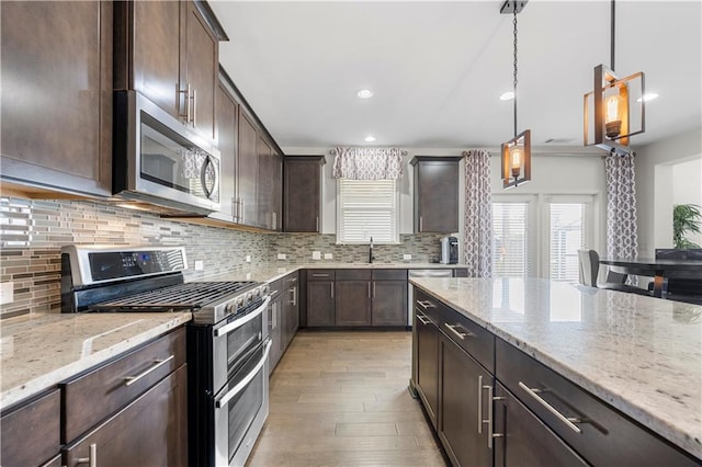 kitchen featuring hanging light fixtures, light stone counters, stainless steel appliances, light hardwood / wood-style flooring, and dark brown cabinetry