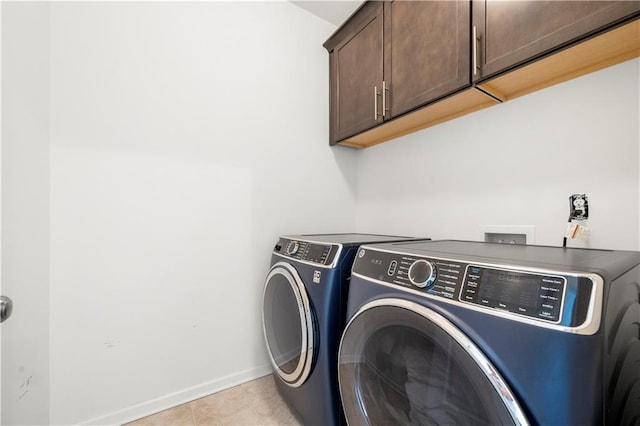 clothes washing area with cabinets, light tile patterned floors, and washer and clothes dryer