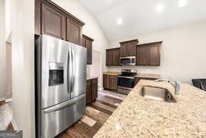 kitchen with light stone counters, appliances with stainless steel finishes, vaulted ceiling, dark wood-type flooring, and sink