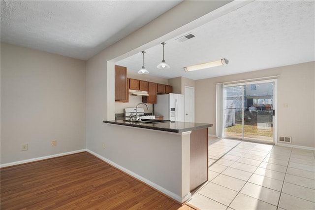 kitchen featuring pendant lighting, sink, white fridge with ice dispenser, kitchen peninsula, and a textured ceiling