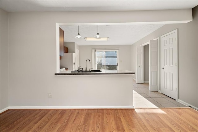 kitchen featuring pendant lighting, kitchen peninsula, sink, and white fridge with ice dispenser