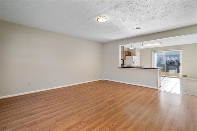 unfurnished living room featuring sink, a textured ceiling, and light hardwood / wood-style flooring