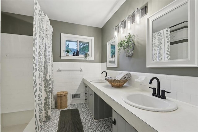 bathroom featuring tile patterned floors, tile walls, double vanity, a wainscoted wall, and curtained shower