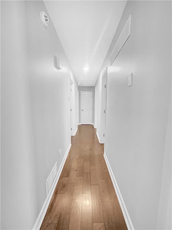 corridor with baseboards, attic access, visible vents, and wood finished floors