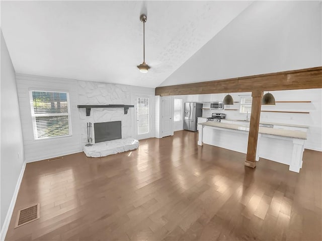 unfurnished living room with dark wood-style floors, visible vents, high vaulted ceiling, and a stone fireplace