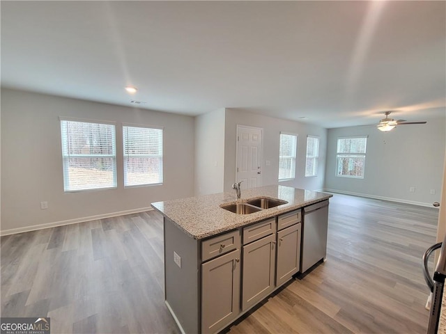 kitchen featuring sink, gray cabinetry, stainless steel dishwasher, light stone counters, and a center island with sink