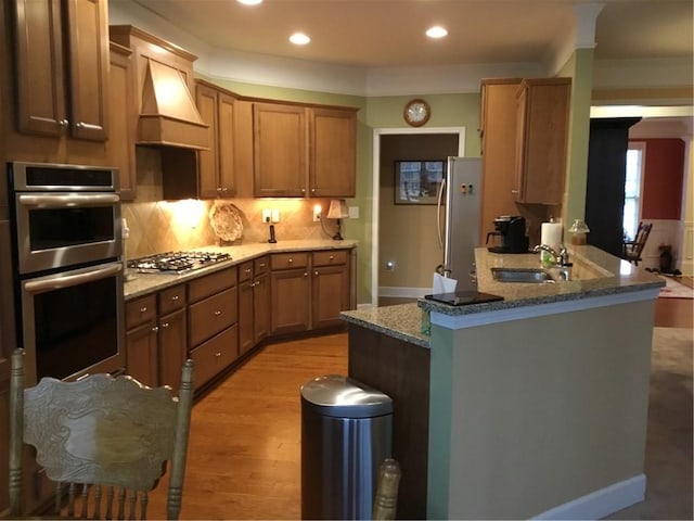 kitchen featuring sink, appliances with stainless steel finishes, light hardwood / wood-style floors, custom range hood, and kitchen peninsula