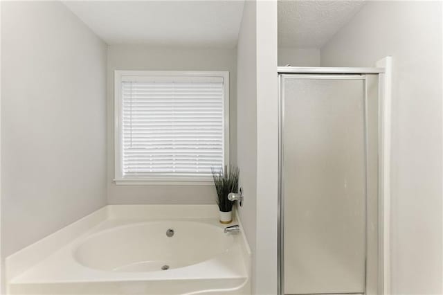 full bath with a textured ceiling, a stall shower, and a bath