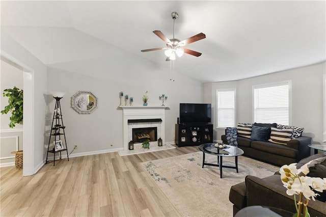 living room with a high end fireplace, light wood finished floors, baseboards, ceiling fan, and vaulted ceiling