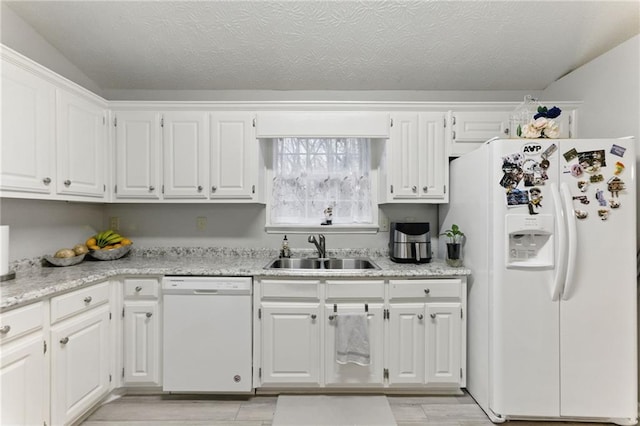 kitchen with a sink, a textured ceiling, white appliances, white cabinets, and light wood finished floors