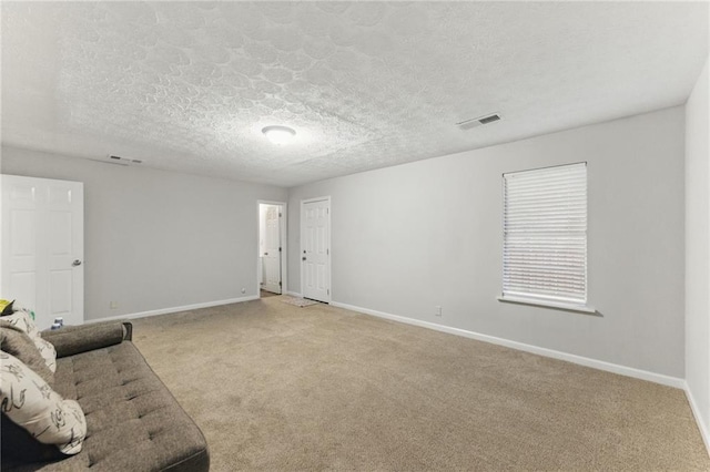 unfurnished living room featuring visible vents, light colored carpet, a textured ceiling, and baseboards