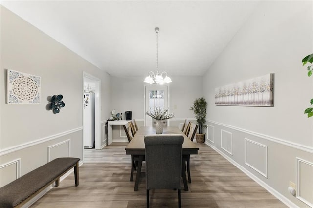 dining room with an inviting chandelier, a decorative wall, light wood-style floors, and vaulted ceiling