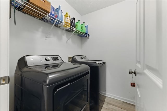 laundry area with baseboards, laundry area, light wood-style floors, a textured ceiling, and washer and clothes dryer