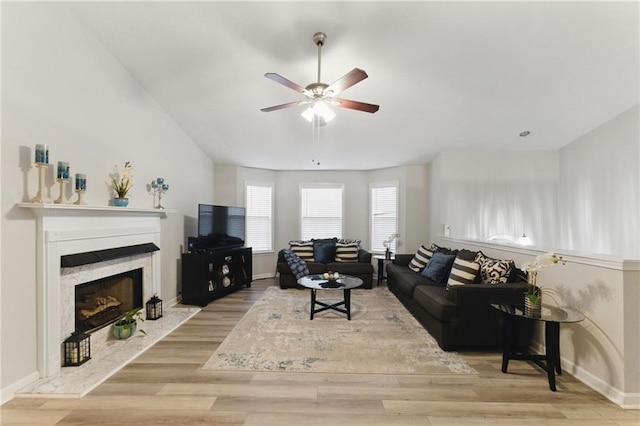 living room featuring a premium fireplace, baseboards, wood finished floors, and a ceiling fan