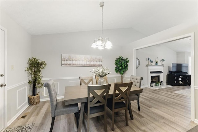 dining room featuring visible vents, a fireplace with raised hearth, light wood-style flooring, and lofted ceiling