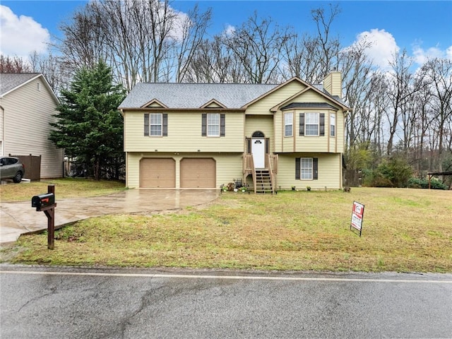 raised ranch featuring a chimney, a front lawn, an attached garage, and driveway