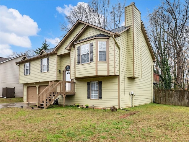 bi-level home featuring a garage, driveway, a front lawn, and fence