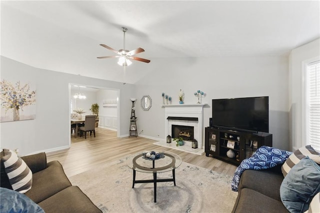 living area featuring ceiling fan with notable chandelier, lofted ceiling, wood finished floors, and baseboards