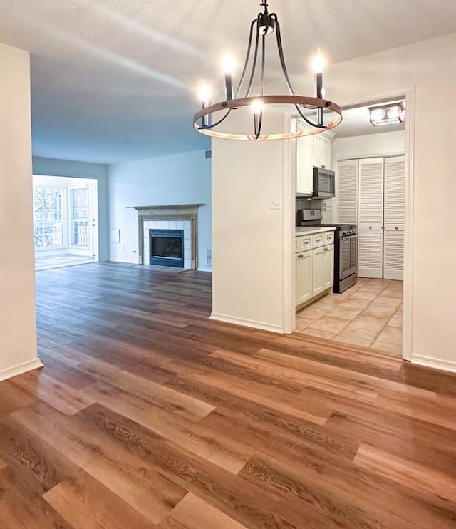 kitchen with a tile fireplace, decorative light fixtures, white cabinets, stainless steel appliances, and light hardwood / wood-style flooring