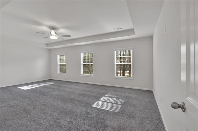 unfurnished room with baseboards, visible vents, dark colored carpet, and a tray ceiling