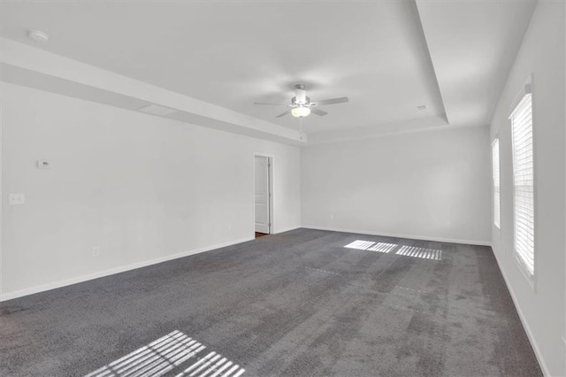 unfurnished room featuring baseboards, dark carpet, a raised ceiling, and a ceiling fan