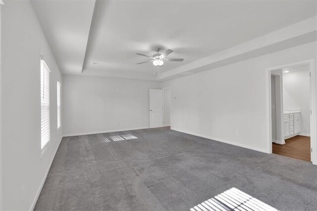 unfurnished room with ceiling fan, baseboards, a tray ceiling, and dark carpet