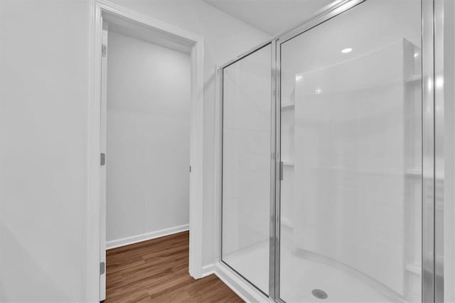 full bath featuring a shower stall, baseboards, and wood finished floors