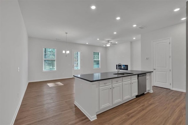 kitchen with a sink, white cabinetry, stainless steel dishwasher, dark countertops, and a center island with sink