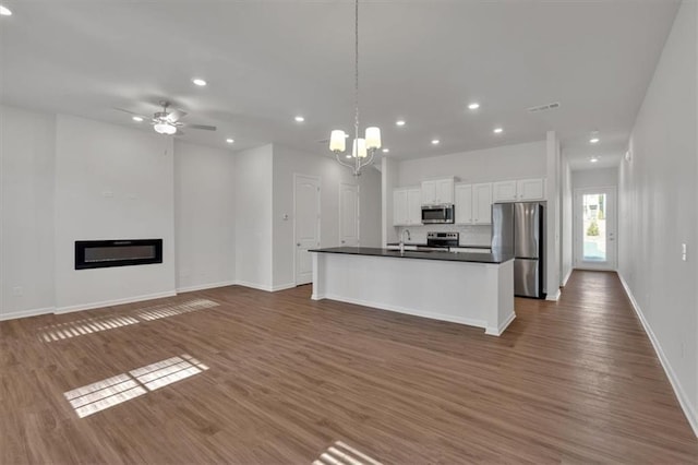 kitchen with white cabinets, open floor plan, appliances with stainless steel finishes, an island with sink, and dark countertops