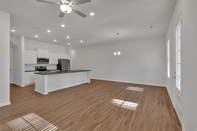 kitchen featuring white cabinetry, open floor plan, hanging light fixtures, appliances with stainless steel finishes, and dark countertops