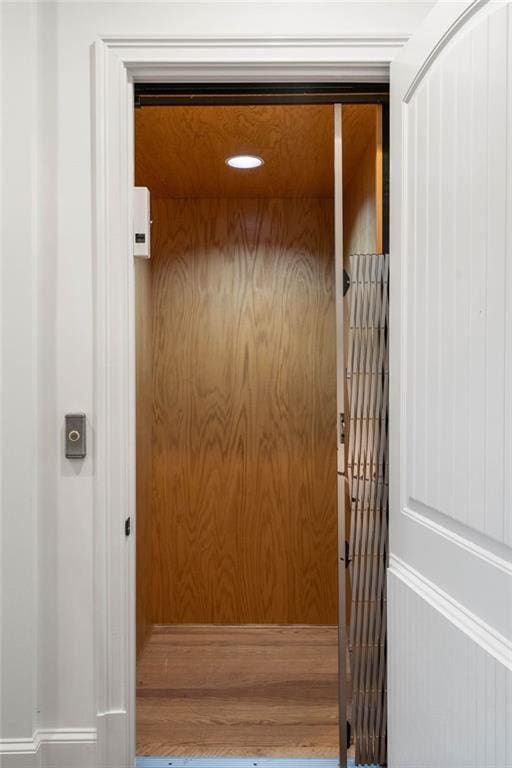 interior details featuring elevator, wood-type flooring, and wood walls