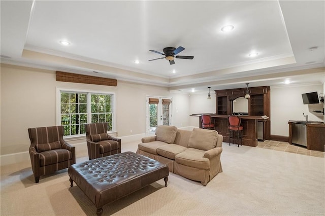 carpeted living room with ornamental molding, indoor bar, a tray ceiling, and ceiling fan