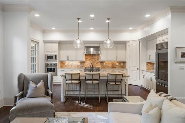 kitchen with a center island with sink, appliances with stainless steel finishes, extractor fan, pendant lighting, and light stone counters