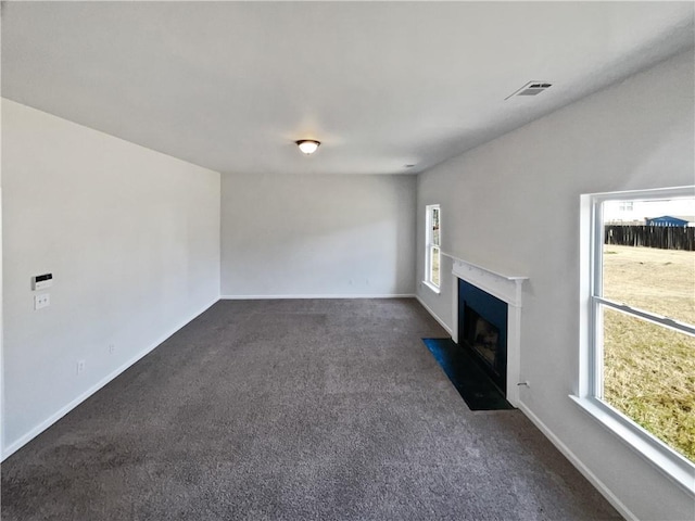 unfurnished living room featuring a healthy amount of sunlight and dark carpet