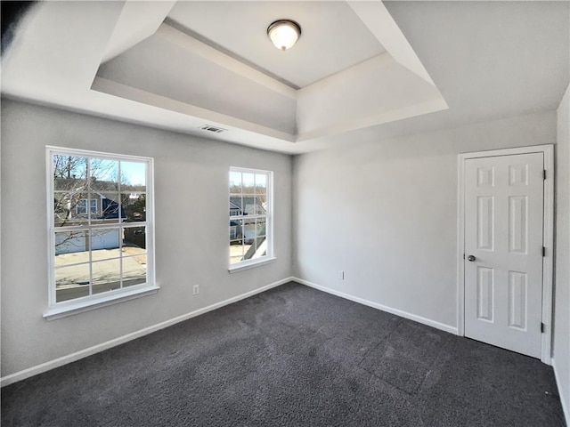 spare room with a raised ceiling and dark colored carpet