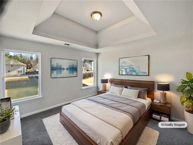 bedroom with a raised ceiling, dark colored carpet, and multiple windows