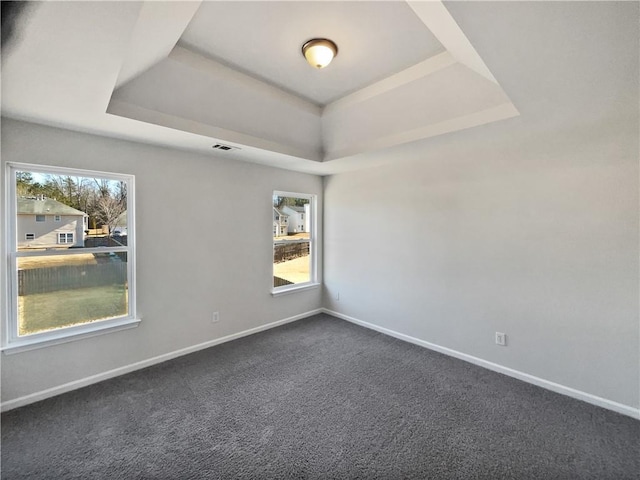 empty room featuring a healthy amount of sunlight, a tray ceiling, and dark colored carpet