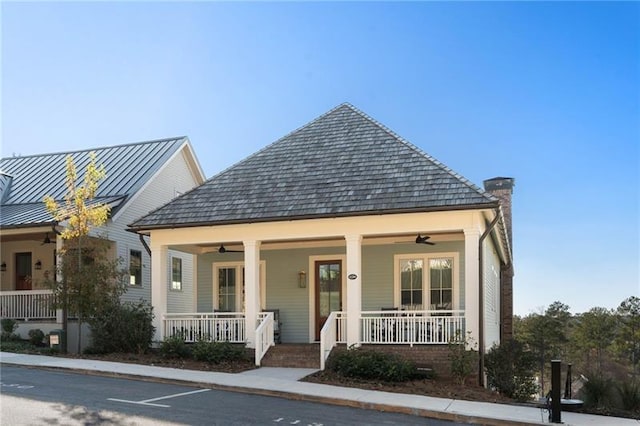 bungalow-style house featuring a standing seam roof, covered porch, metal roof, ceiling fan, and a chimney