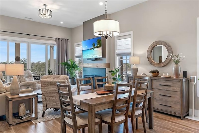 dining area with an inviting chandelier, light wood-style flooring, a fireplace, and visible vents