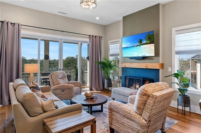 living room featuring a wealth of natural light, visible vents, a lit fireplace, and wood finished floors