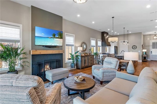 living area with recessed lighting, baseboards, a warm lit fireplace, and wood finished floors