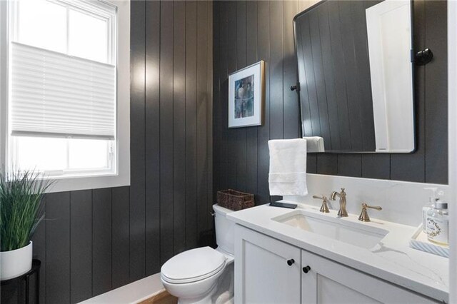 bathroom featuring wood walls, vanity, and toilet