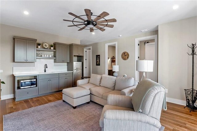 living room featuring light hardwood / wood-style flooring, ceiling fan, and sink