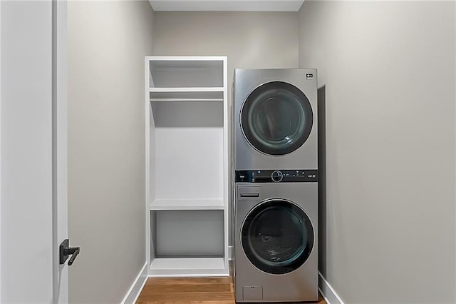 laundry area featuring stacked washer / dryer, laundry area, baseboards, and wood finished floors