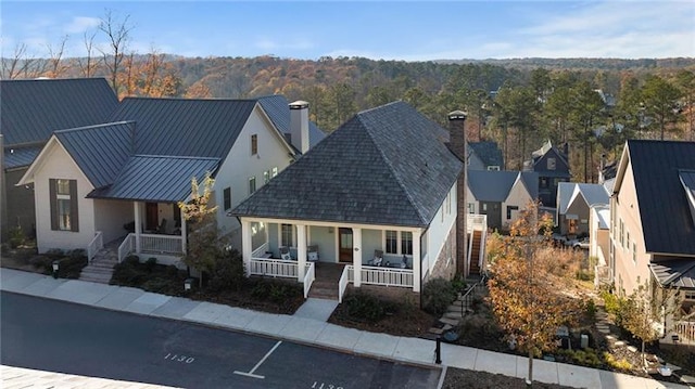 view of front facade with a standing seam roof, covered porch, a chimney, stairs, and metal roof