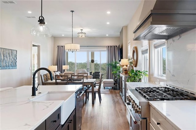 kitchen with hardwood / wood-style flooring, wall chimney exhaust hood, light stone countertops, decorative light fixtures, and stainless steel appliances