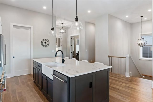 kitchen with sink, an island with sink, stainless steel dishwasher, and hardwood / wood-style flooring