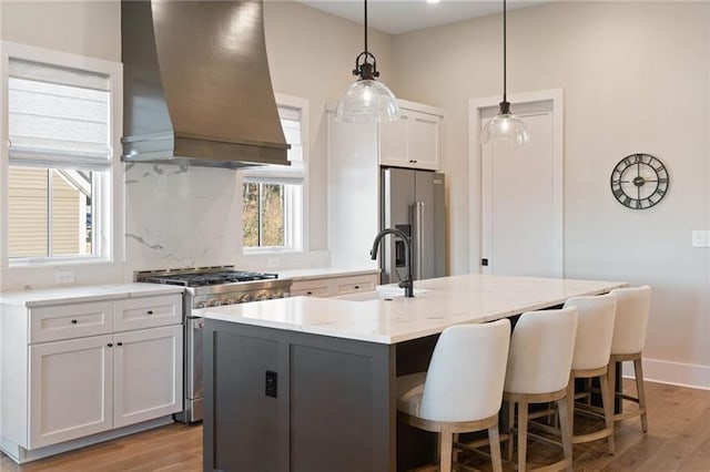 kitchen with pendant lighting, premium range hood, an island with sink, premium appliances, and white cabinetry